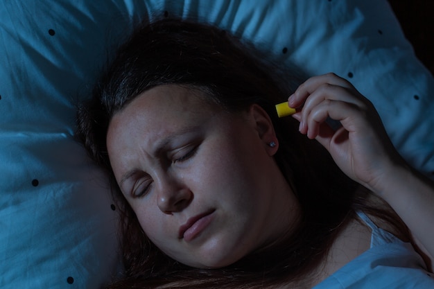 Jeune Femme Mettant Des Bouchons D'oreille Dans Ses Oreilles Pour La Réduction Du Bruit Avant De Dormir, L'insomnie