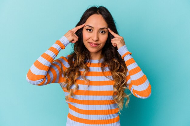 Jeune Femme Mexicaine Isolée Sur Fond Bleu Concentrée Sur Une Tâche, Gardant Les Index Pointant La Tête.