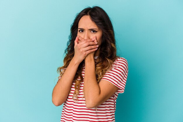 Jeune femme mexicaine isolée sur fond bleu couvrant la bouche avec les mains à la peur.