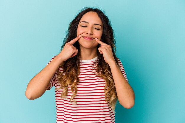 Jeune femme mexicaine isolée sur fond bleu doutant entre deux options.