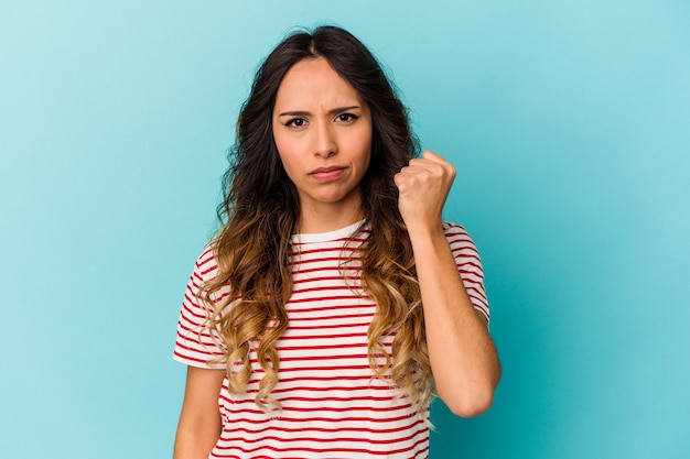 Jeune femme mexicaine isolée sur fond bleu montrant le poing à la caméra, expression faciale agressive.