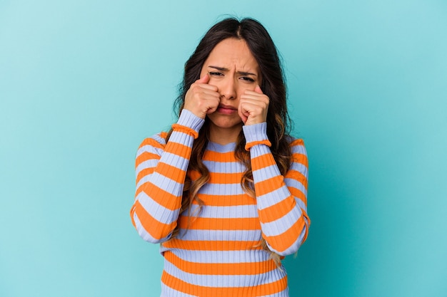 Jeune femme mexicaine isolée sur fond bleu pleurnichant et pleurant de manière inconsolable.