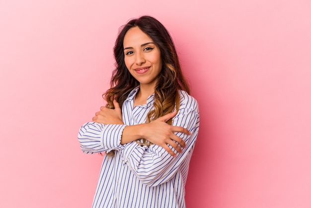 Jeune femme mexicaine isolée sur fond rose câlins, souriante insouciante et heureuse.