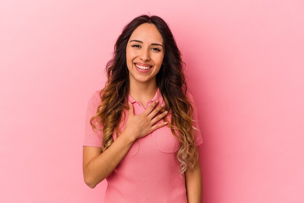 Jeune femme mexicaine isolée sur fond rose éclate de rire en gardant la main sur la poitrine.