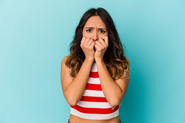 Jeune femme mexicaine isolée sur le mur bleu se mordant les ongles, nerveuse et très anxieuse.