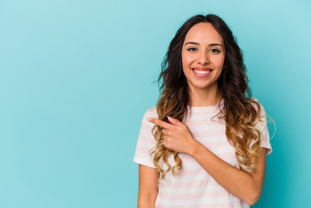 Jeune femme mexicaine isolée sur mur bleu souriant et pointant de côté, montrant quelque chose à l'espace vide.