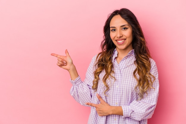 Jeune femme mexicaine isolée sur mur rose excité pointant avec l'index loin.