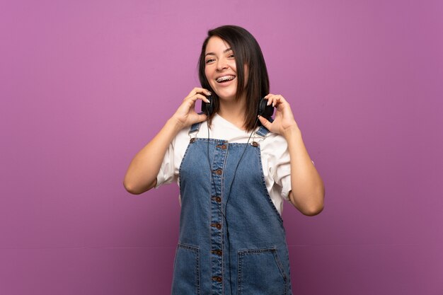 Jeune femme mexicaine sur mur isolé, écouter de la musique avec des écouteurs