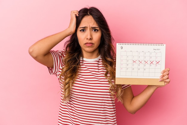 Jeune femme mexicaine tenant un calendrier isolé sur fond rose étant choquée, elle s'est souvenue d'une réunion importante.