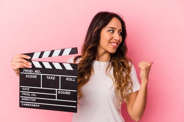 Jeune femme mexicaine tenant clap isolé sur fond rose points avec le pouce, riant et insouciant.