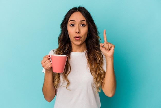 Jeune femme mexicaine tenant une tasse isolée sur un mur bleu ayant une excellente idée, concept de créativité.