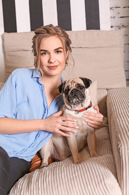 Jeune femme avec mignon chien carlin sur le canapé à la maison.