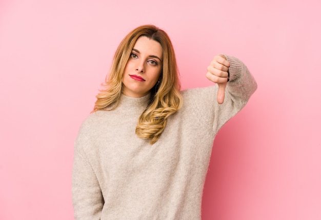 Jeune femme mignonne blonde portant un pull isolé montrant un geste d'aversion, les pouces vers le bas. Concept de désaccord.