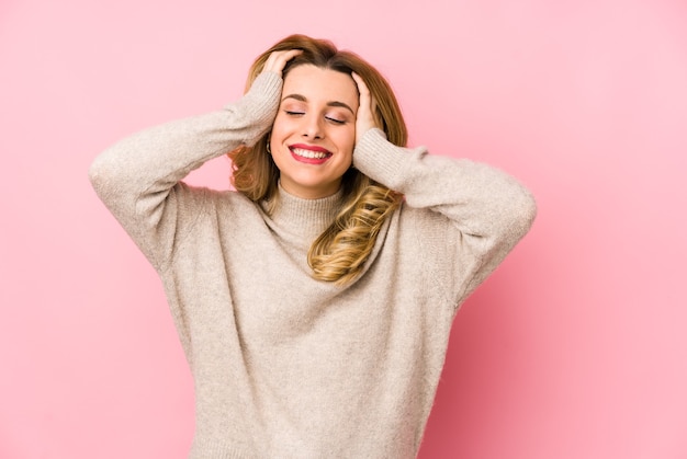 Jeune femme mignonne blonde portant un pull isolé rit joyeusement en gardant les mains sur la tête. Concept de bonheur.