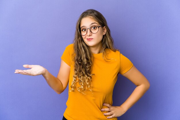 Jeune femme mignonne caucasienne doutant et haussant les épaules dans le geste de questionnement.