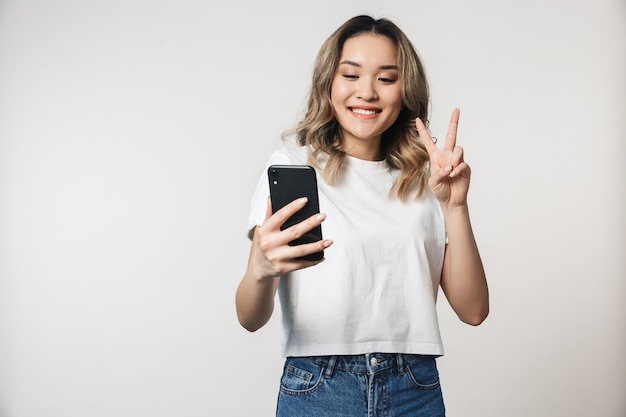 Jeune femme mignonne émotionnelle posant isolée sur un mur blanc parlant par téléphone portable