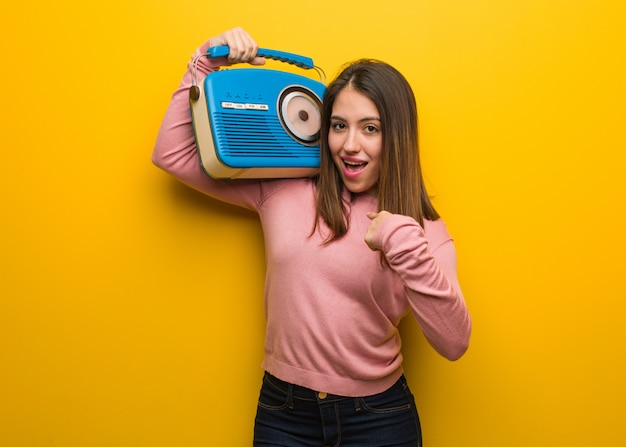 Jeune femme mignonne tenant une radio vintage surprise, réussie et prospère