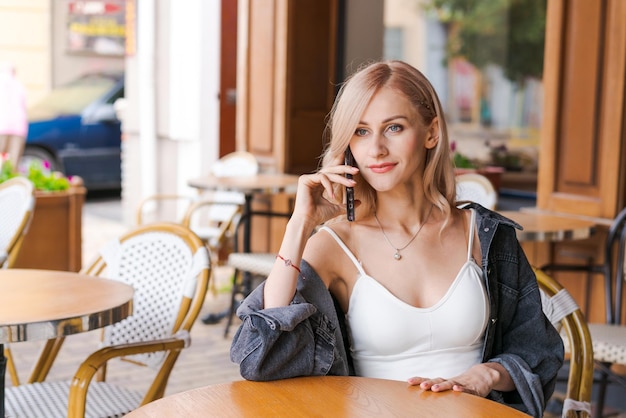 Une jeune femme mignonne utilisant un téléphone est assise dans un café à table avec un smartphone répondant