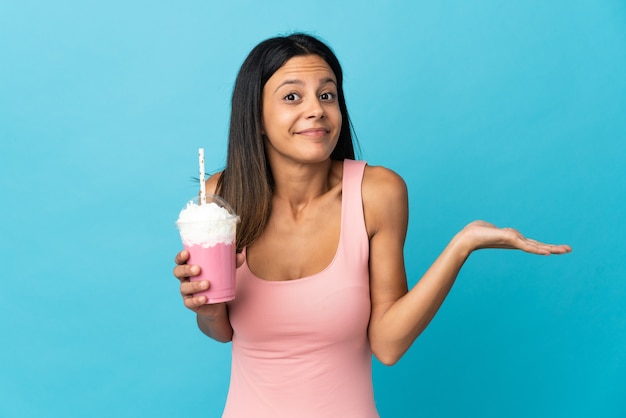 Jeune femme avec milk-shake aux fraises ayant des doutes tout en levant les mains