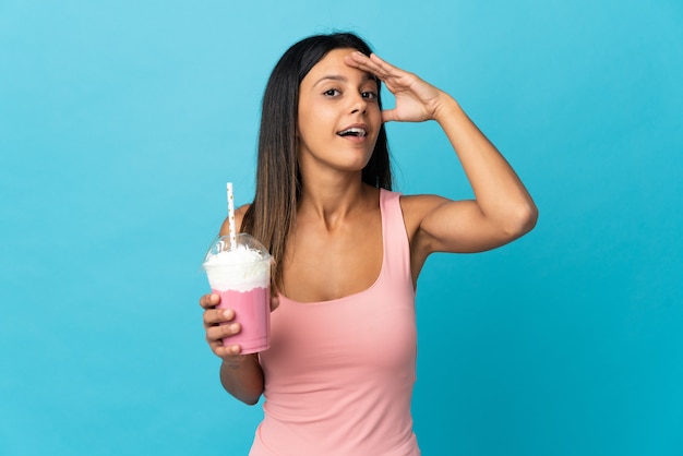 Jeune femme avec milk-shake aux fraises faisant un geste de surprise tout en regardant sur le côté