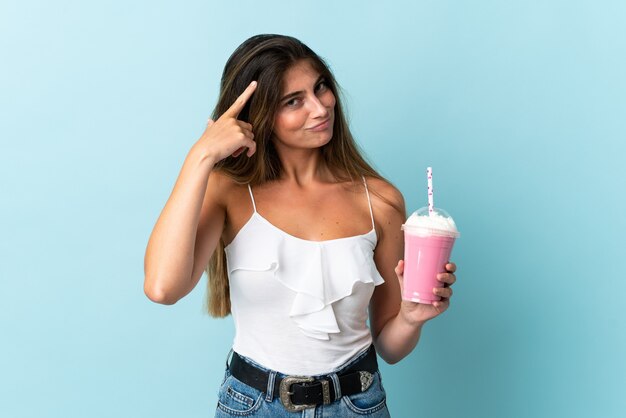 Jeune femme avec milk-shake aux fraises isolé sur mur bleu ayant des doutes et de la pensée