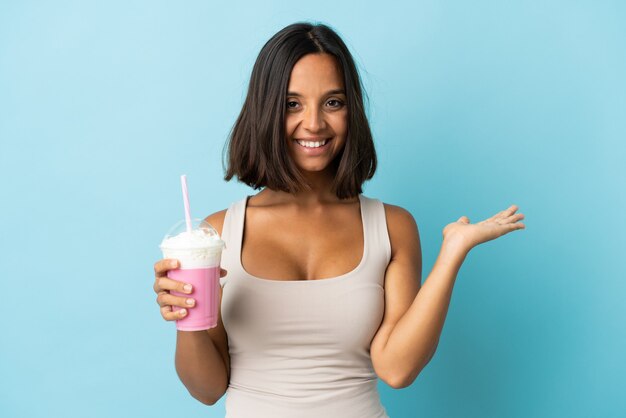 Jeune femme avec milk-shake aux fraises isolé sur mur bleu holding copyspace imaginaire sur la paume pour insérer une annonce