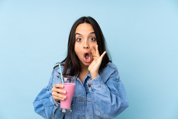 Jeune femme avec milk-shake aux fraises sur mur bleu isolé criant et annonçant quelque chose