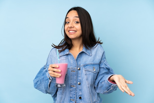 Jeune femme avec milk-shake aux fraises sur mur bleu isolé souriant