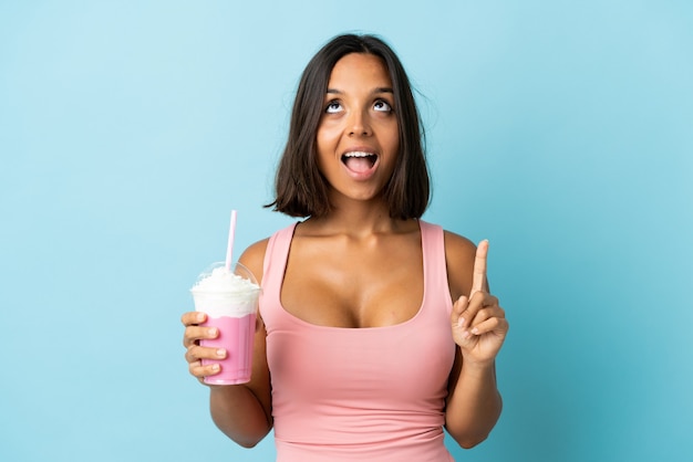 Jeune femme avec milkshake aux fraises sur bleu pointant vers le haut et surpris