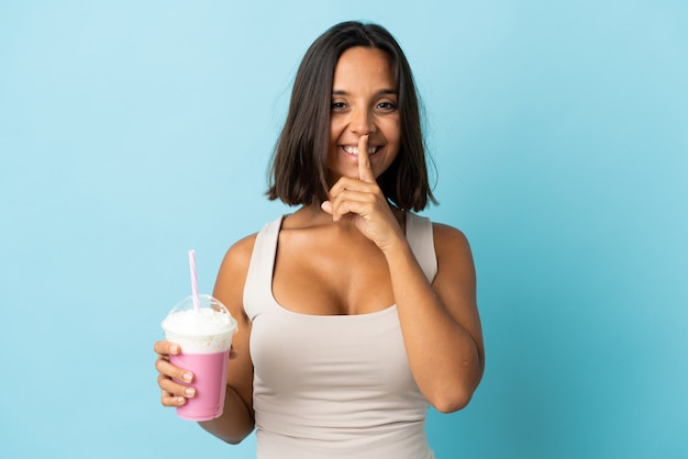 Jeune femme avec milkshake aux fraises isolé sur bleu montrant un signe de silence geste mettant le doigt dans la bouche