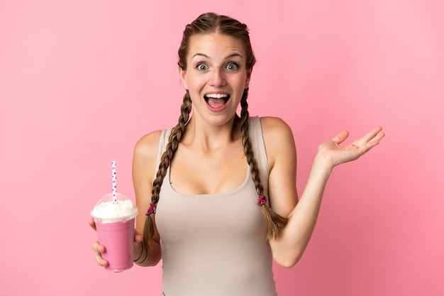 Jeune femme avec milkshake aux fraises isolé sur fond rose avec une expression faciale choquée