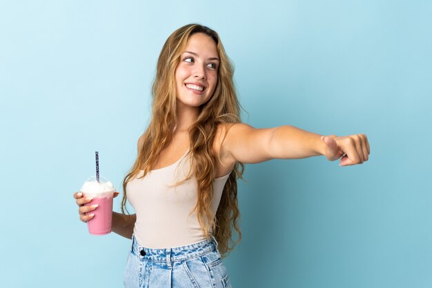 Jeune femme avec milkshake aux fraises isolé sur mur bleu donnant un geste de pouce en l'air