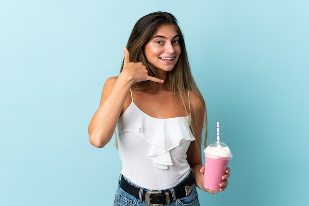 Jeune femme avec milkshake aux fraises isolé sur mur bleu faisant le geste du téléphone. Rappelez-moi signe