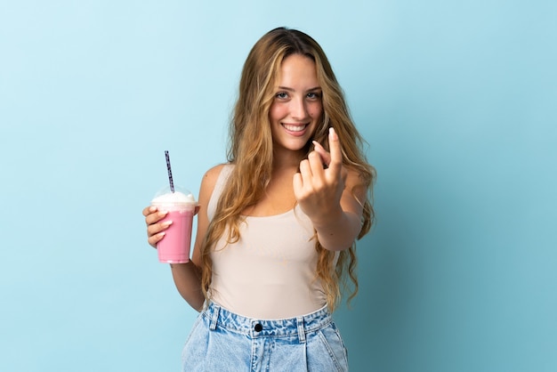 Jeune femme avec milkshake aux fraises isolé sur mur bleu faisant le geste à venir