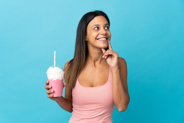 Jeune femme avec milkshake aux fraises pensant une idée tout en levant