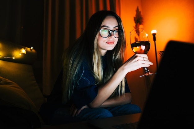 Jeune femme millénaire ayant un appel vidéo sur un ordinateur portable et buvant du vin, utilise la technologie pour communiquer avec ses amis ou sa famille.