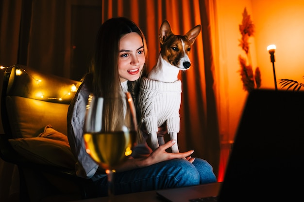 Jeune femme millénaire avec son chien ayant un appel vidéo sur un ordinateur portable et buvant du vin, utilise la technologie pour communiquer avec ses amis ou sa famille.