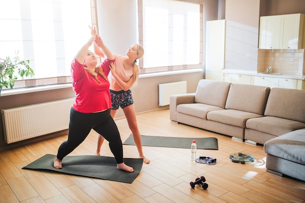 Jeune femme mince bien construite aider plus modèle de taille pour s'étirer et faire de l'exercice dans le salon