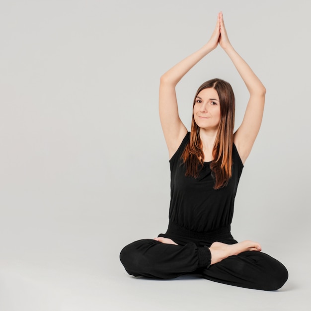 Jeune femme mince brune en noir assis en position du lotus au yoga