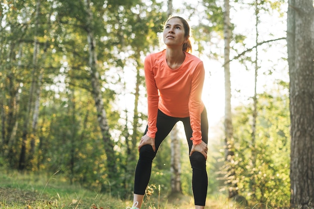 Jeune femme mince brune en vêtements de sport courant dans la forêt à l'heure du lever du soleil d'or Santé et bien-être mode de vie fitness