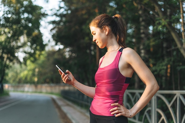 Jeune Femme Mince Brune En Vêtements De Sport Courir Et Utiliser Un Téléphone Portable Au Parc D'automne à L'heure Du Lever Du Soleil à L'heure D'or Santé Et Bien-être Mode De Vie De Remise En Forme