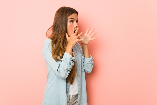 Jeune femme mince crie fort, garde les yeux ouverts et les mains tendues.