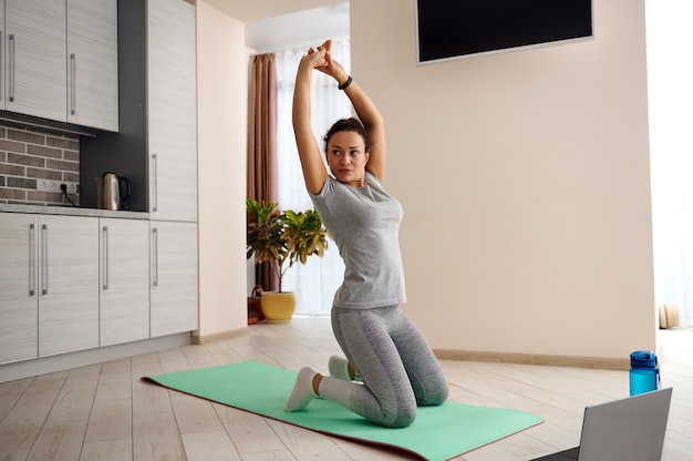 Jeune femme mince fit étirant son corps debout sur un tapis de fitness. Femme travaillant à la maison