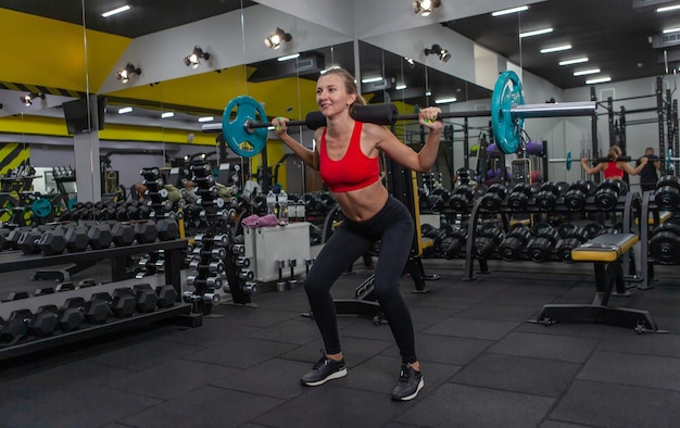 Jeune femme mince pratiquant des squats avec une barre sur ses épaules dans une salle de sport moderne