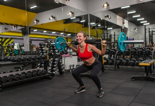 Jeune femme mince pratiquant des squats avec une barre sur ses épaules dans une salle de sport moderne