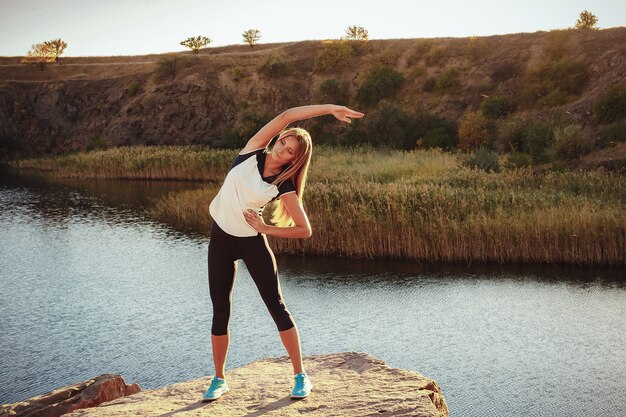 Jeune femme mince, pratiquer le yoga en plein air sur le rivage de pierre de la rivière de montagne. Unité avec le concept de la nature