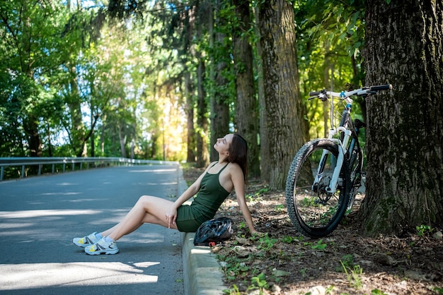 Jeune femme mince en robe verte sur vélo debout sur la route et se reposer après le voyage