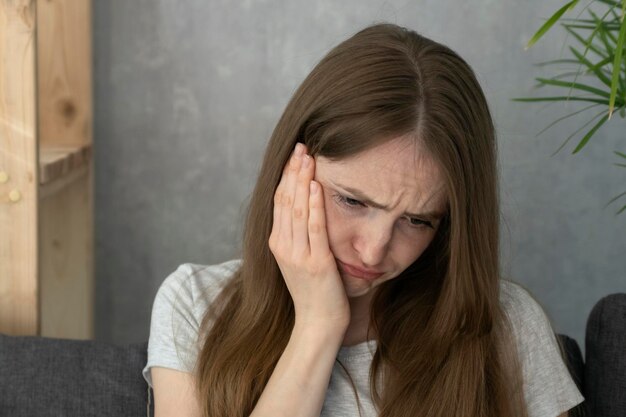Jeune femme a mis sa main sur sa joue et souffre de maux de dents. Problèmes dentaires chez l'adulte.