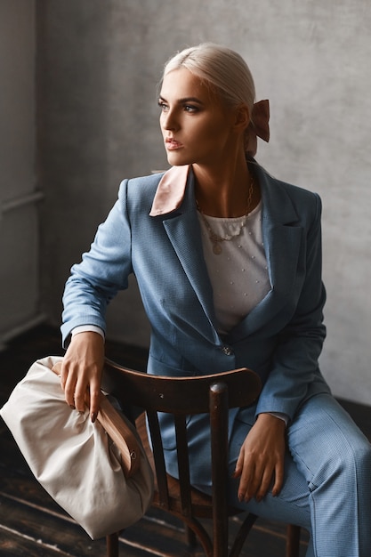 Une jeune femme à la mode avec des cheveux blonds parfaits dans un élégant costume bleu qui pose en studio
