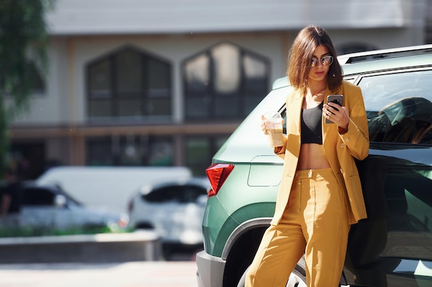 Jeune femme à la mode en manteau de couleur bordeaux pendant la journée avec sa voiture